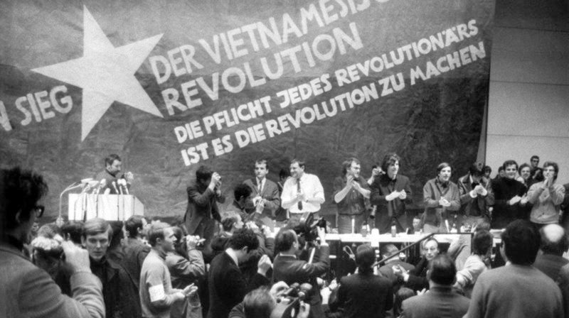 17.02.1968, Berlin: Etwa 3000 Personen, meist Studenten, nehmen an der vom Sozialistischen Deutschen Studentenbund (SDS) durchgeführten «Internationalen Vietnam-Konferenz» in der TU teil. Auf dem Bild vor einer übergroßen Vietkong-Fahne am Tisch stehend sind zu sehen:v.l.n.r. K.D. Wolff (am Rednerpult), Dr. Klaus Meschkat, Dr. Johannes Agnoli, Christian Semmler, Gaston Salvatore, Rudi Dutschke, Günther Ament, Kurt Steinhaus und Tariq Ali. Mit dem Vietnam-Kongress vor 50 Jahren erreichte der Studentenprotest in Deutschland seinen politischen Höhepunkt. – Bild: WDR/​dpa/​Volkmar Hoffmann